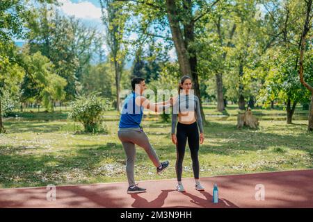 A male sportsperson is holding his female friend shoulder while doing some leg exercises Stock Photo