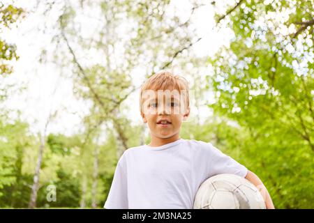 Portrait of smiling boy carrying soccer ball while standing in park Stock Photo