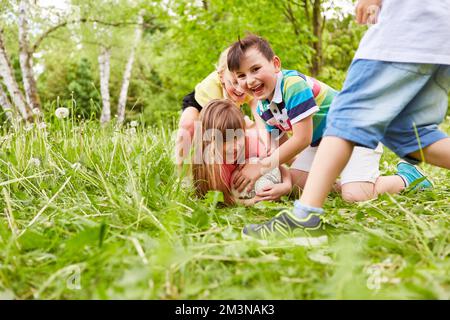 Group of children playing soccer and scuffling around football in the grass