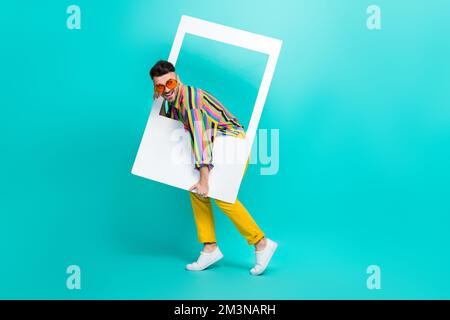 Full body size photo of young overjoyed hipster guy wear striped retro shirt hold paper frame take shot event isolated on aquamarine color background Stock Photo