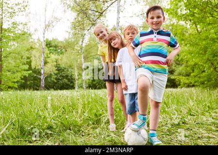 Portrait of smiling boy standing on football by male and female friends in park Stock Photo