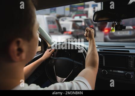 Novice driver sitting in his car behind the wheel shaking his fist threatens another motorist. Bad and aggressive behavior on road concept. Stock Photo