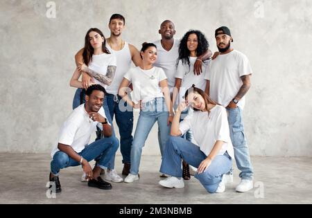 Multiethnic group of happy friends. Diverse young people standing together in white shirts and jeans on minimalistic background in studio Stock Photo