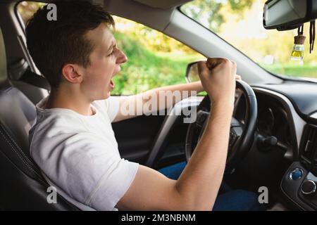 Novice driver screaming sitting in his car behind the wheel shaking his fist threatens another motorist. Bad and aggressive behavior on road concept. Stock Photo