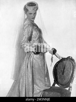 A wedding dress of pale gold and ivory patterned brocade with a prettily folded bodice and a train cut in one with the skirt.  The long, tight-fitting sleeves are cuffed with mink.     Date: 1953 Stock Photo