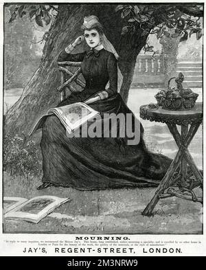 A pensive woman sits beneath a tree, modelling mourning attire from Jay's of London. Her work basket is perched on a rustic table, and illustrated magazines lie discarded at her feet.     Date: 1888 Stock Photo