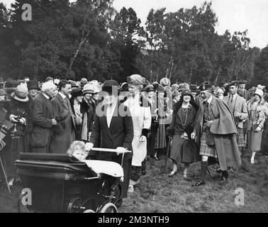 The Silver Jubilee of King George V. The Royal Family at a garden party at Balmoral Castle on September 10th 1927. The two future Kings, Edward the VIII and George the VI walk behind their father with the Duchess of York, the future Queen Elizabeth, the Queen Mother sharing a joke with King George V. The future Queen Elizabeth II is seen in a pram pushed by her nanny, Clara Knight.  Queen Mary walks directly behind. Stock Photo