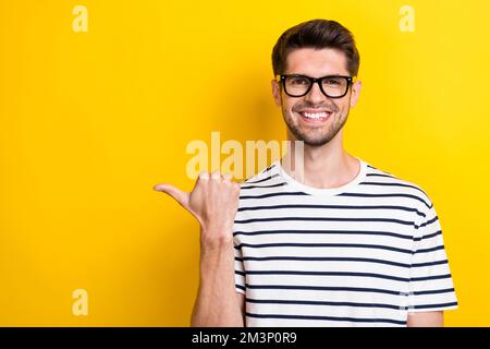 Portrait of cheerful positive person beaming smile indicate thumb finger empty space isolated on yellow color background Stock Photo