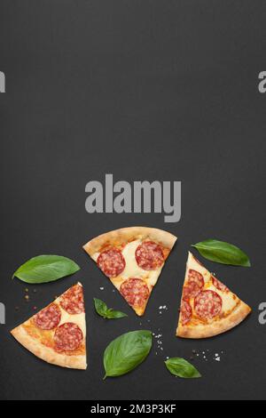 slices of pepperoni pizza with basil and spices on a black background Stock Photo