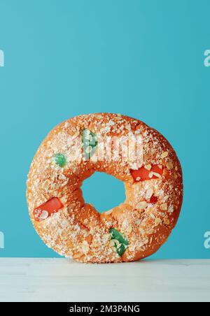 the spanish three kings cake, called roscon de reyes, eaten traditionally on epiphany day, standing on a white table against a blue background with so Stock Photo