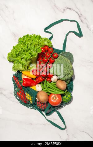 Green shopping bag with groceries on a gray marble background. Eco friendly packaging. Stock Photo