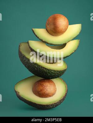 Balancing avocado slices on green background Stock Photo