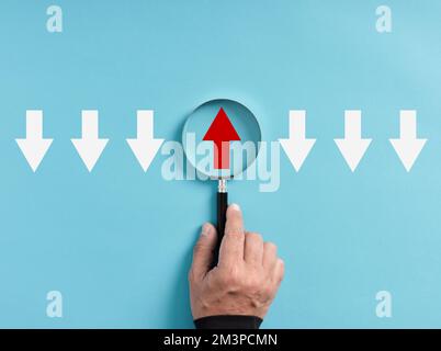 Focusing on business growth trend, development opportunity or positive aspects. Hand holds magnifying glass focusing on the red up arrow with differen Stock Photo