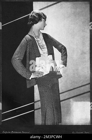 A black and white tweed suit in Chanel's inimitable manner, with fitted hips and pleated skirt.  A narrow belt marks the waist line of the white gilet.       Date: 1929 Stock Photo