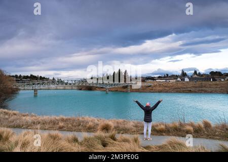 Tourist pose at the Maclaren Foot Bridge in late winter with beautiful turquoise color Lake Tekapo. Canterbury, New Zealand South Island. Stock Photo