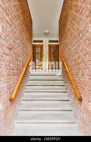 some stairs leading up to the front door on a brick building with wood railings and wooden handrails Stock Photo