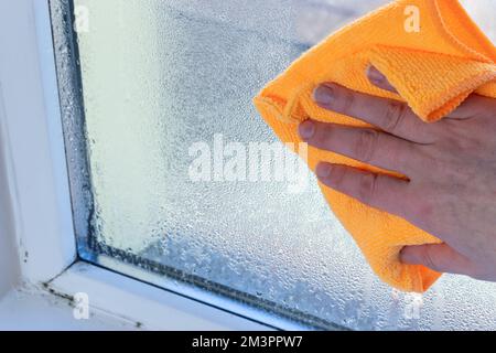 hand wipes off water condensation from plastic window glass in the room Stock Photo