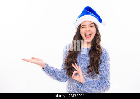 Winter teen girl pointing on copy scpace. Christmas teen girl. Portrait of teenager in winter sweater isolated over white background. Stock Photo