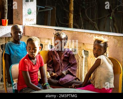 MBOUR, SENEGAL - DECEMBER, Circa, 2020. Unidentified group of cheerful children sitting on chairs outdoors, looking at teacher to learn song with musi Stock Photo