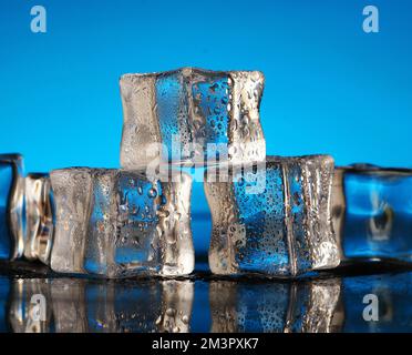 three ice cubes in drops on a blue background Stock Photo