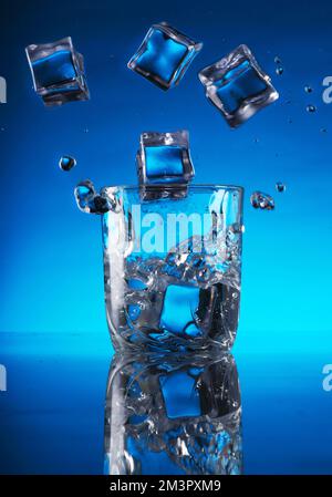 ice cubes falling into a glass of water on a blue background Stock Photo