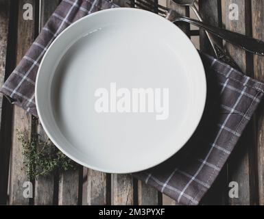 White empty plate or bowl on rustic and wooden background with old fashioned spoon and fork Stock Photo