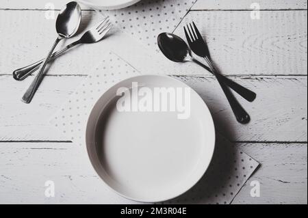 Empty white plate with fork and spoon on abstract, white, matte background Stock Photo