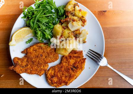 milanesa steak or breaded schnitzel served on dish with green salad and cooked potato salad on wooden table. homemade simple lunch Stock Photo