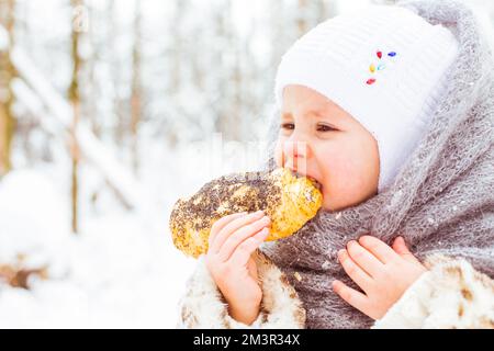 Girl in the winter forest eats delicious bun Stock Photo