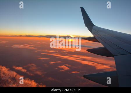 View from an airplane window showing a plane wing with orange sky at sunset Stock Photo