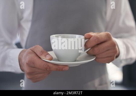 Your coffee, please. Cropped image of a man holding a cup of good coffee against the background of a gray apron. With a space to copy. High quality photo Stock Photo