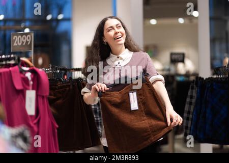 Shopping in secondhand. Happy smiling young Caucasian woman find best skirt. Concept of thrift store and sale. Stock Photo