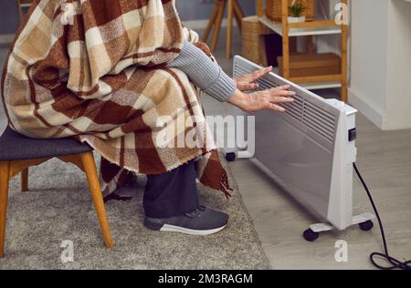 Man sitting at home in winter, feeling cold and warming up his hands by an electric heater Stock Photo