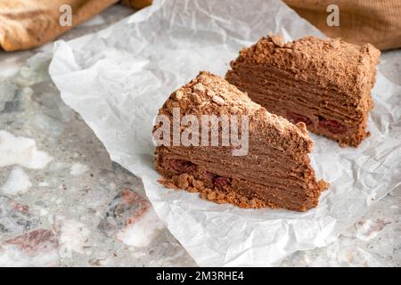 Napoleon cake with custard is decorated with cherries and grated chocolate on table. Dessert Napoleon cake is chopped. Cake Napoleon close-up. Stock Photo
