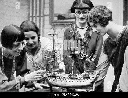 Four women poring over a model ship on display at an exhibition of old ships and maps. At the time these were popular themes in interior decoration.  1927 Stock Photo