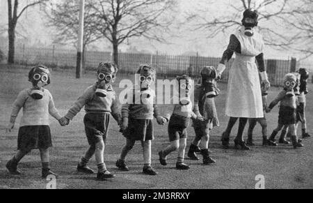 London babies find peace in the country: a nurse walks evacuated children in gas masks across a playground, to accustom them to the wearing of gas masks. LCC Residential School near Windsor.     Date: 1941 Stock Photo