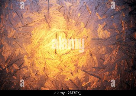 Christmas background with frozen pattern on window glass. Sunrise light glowing throuth icy window. Real texture of winter snowfrost Stock Photo