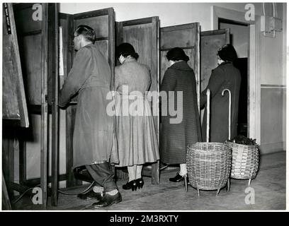 Four people voting in the General Election, 26 May 1955, in Brixton town hall, London. The 1955 General Election, often described as one of the dullest of the post-war period, saw a substantial yet unsurprising increase in the Conservative majority, giving them 345 MPs for the next term. The Conservative party, led for the first time by Antony Eden, proved a stark contrast to the 72 year-old Clement Attlee who continued as the leader of a divided Labour party, and the 1955 Election was the last time the Conservatives dominated the constituencies of Scotland. These people are voting in the cons Stock Photo