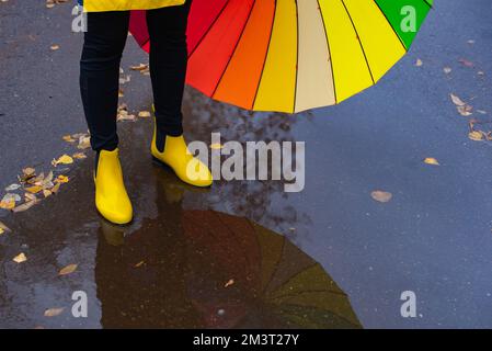 multi-colored umbrella and yellow boots in a puddle Stock Photo