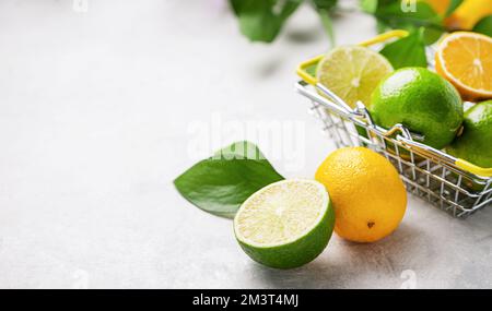Fresh lemons and limes with leaves in a supermarket basket on a light textured background close up. Citrus fruit concept for freshly squeezed lemonade Stock Photo