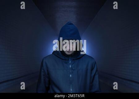 A man in a hood on the street, in a dark alley. Addiction concept. Tinted photo Stock Photo