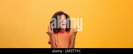 Waist-up shot of amazed happy stylish african american woman feeling awesome rocking on party yelling from joy and satisfaction showing rock n roll Stock Photo