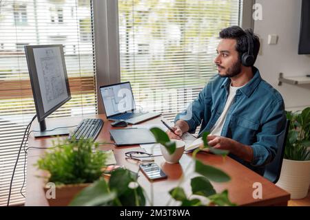 indian male designer in headphones works in home office drawing on graphic tablet Stock Photo