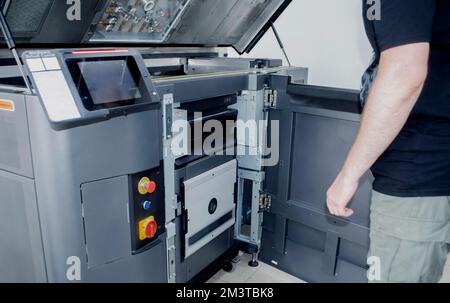 A man worker and a large industrial powder 3d printer in a laboratory in a factory. Multi Jet Fusion. Industrial equipment. New modern 3D printing , additive progressive technology. MJF Stock Photo