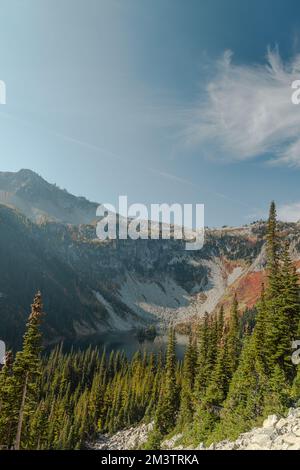 Vertical Photo of lush high mountain altitude massive conifer trees off trail with alpine lake below in the North Cascades National Park in Northern W Stock Photo