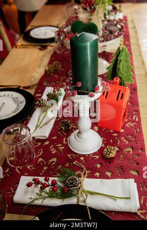 Festive Christmas table setting. On a wooden table lies a red runner, black plates on white says Enjoy, golden forks, spoons, knives. New year green c Stock Photo