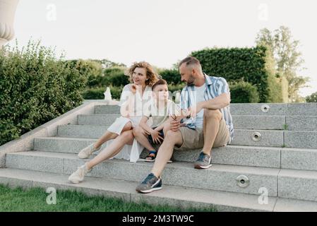 Father, mother, and son are sitting on the steps in the garden of an old town Stock Photo