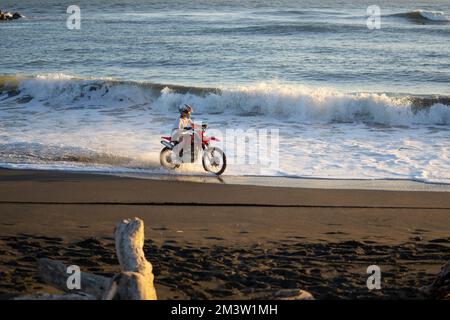 Wanganui New Zealand - April 9 2022; Motorcyclist speeding through water and splashing at waterline on Castlecliff beach at dusk Stock Photo
