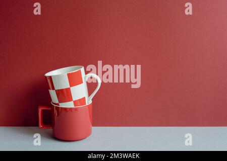 Stack of red mug cups on gray table. red wall background. kitchen and cafe concept Stock Photo