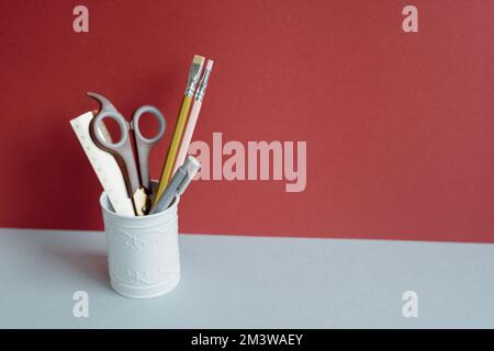 Ruler, scissors, colored pencil, pen in pencil holder case on gray desk. red wall background. copy space Stock Photo